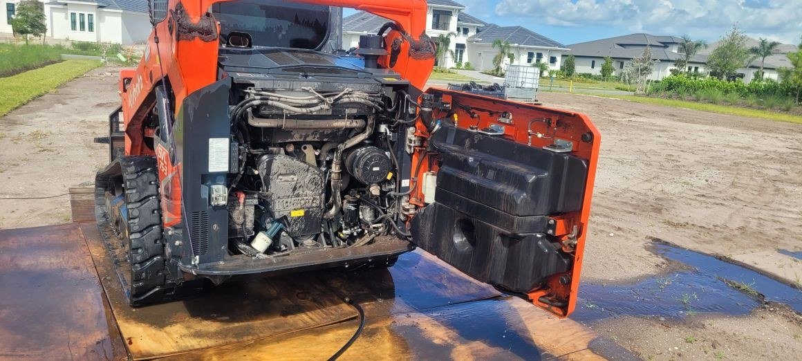 An orange skid-steer being cleaned on site
