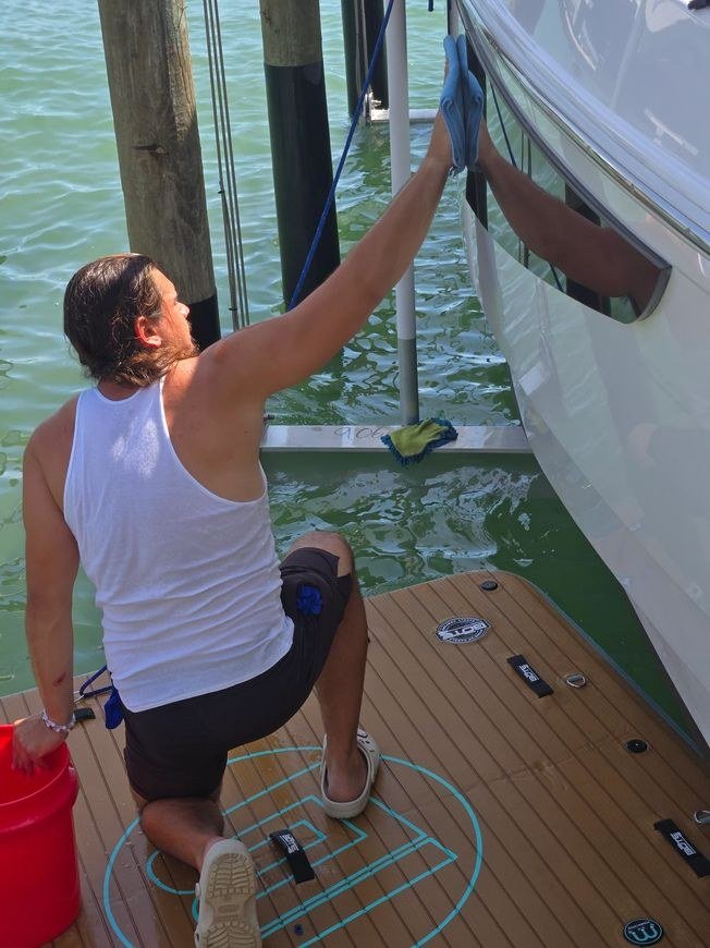 A technician waxing the hull of a boat from the dock