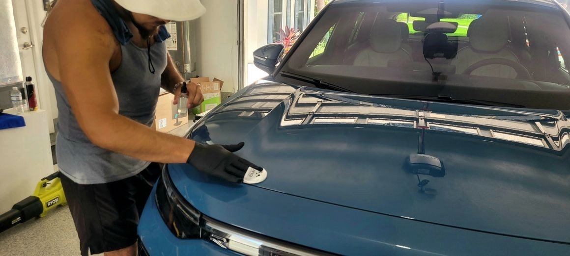 An OnSite AutoBrite technician polishing the hood of a blue car on site