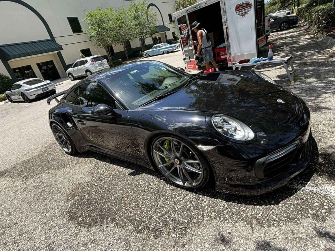 A black Porsche 911 beside the OnSite AutoBrite work trailer